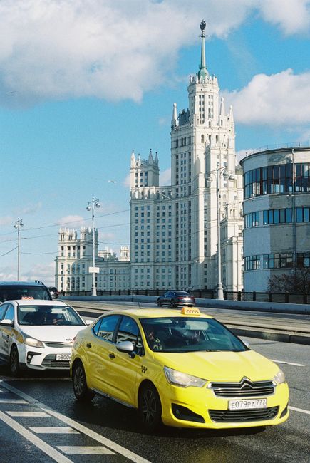 The image depicts a busy city street with a bright yellow taxi in the foreground, displaying a sleek and modern design with a clear roof sign indicating its taxi status. Behind the taxi, several other