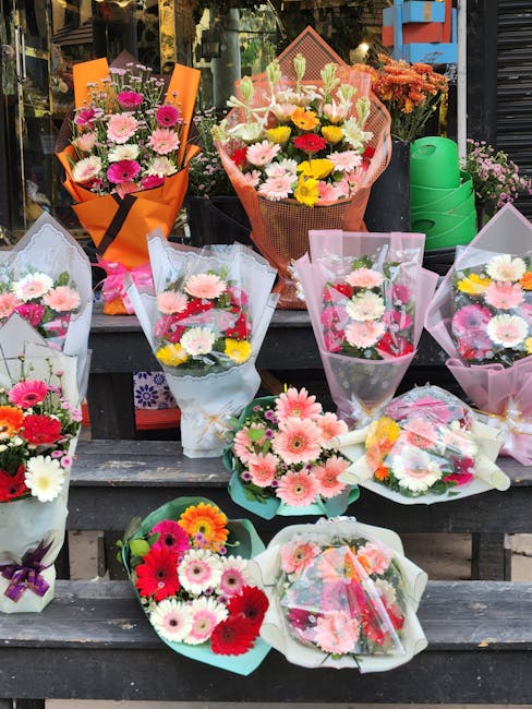 A display of freshly arranged flower bouquets featuring a variety of colorful blooms, including pink, white, yellow, and red daisies, chrysanthemums, and roses, wrapped in pastel-colored and transpare